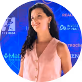Smiling woman with long dark hair wearing a sleeveless pink blouse against a blue background with text and logos.